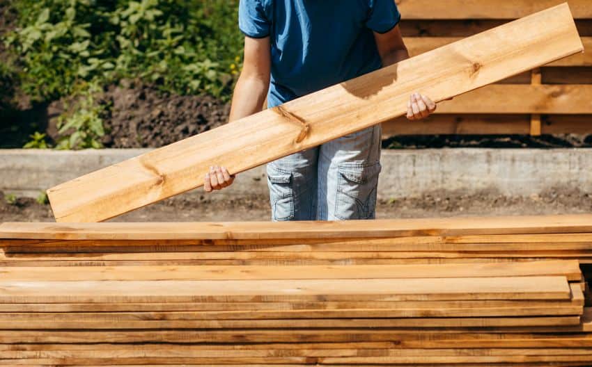 Person holding lumber plank stack outdoor construction site