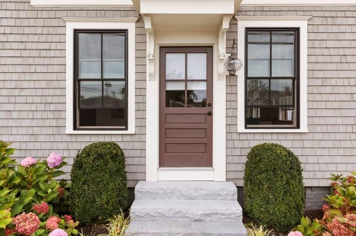 Modern home exterior with brown front door, black windows, gray siding and garden shrubs