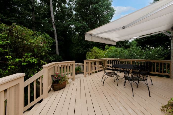 Wood deck patio with railing, outdoor table set, canopy shade, surrounded by lush trees